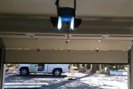 View from inside an Emerson garage showing a newly installed Chamberlain garage door opener with a white service truck parked outside.