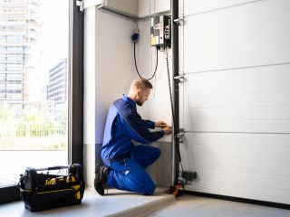 Garage Door Installation Technician – Cartersville GA Technician in blue uniform kneeling beside a newly installed white garage door, adjusting the opener system and hardware in a Cartersville, GA home garage.