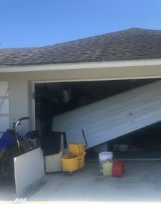Garage door off track and partially collapsed inside a cluttered Adairsville garage, illustrating the need for professional garage door replacement.